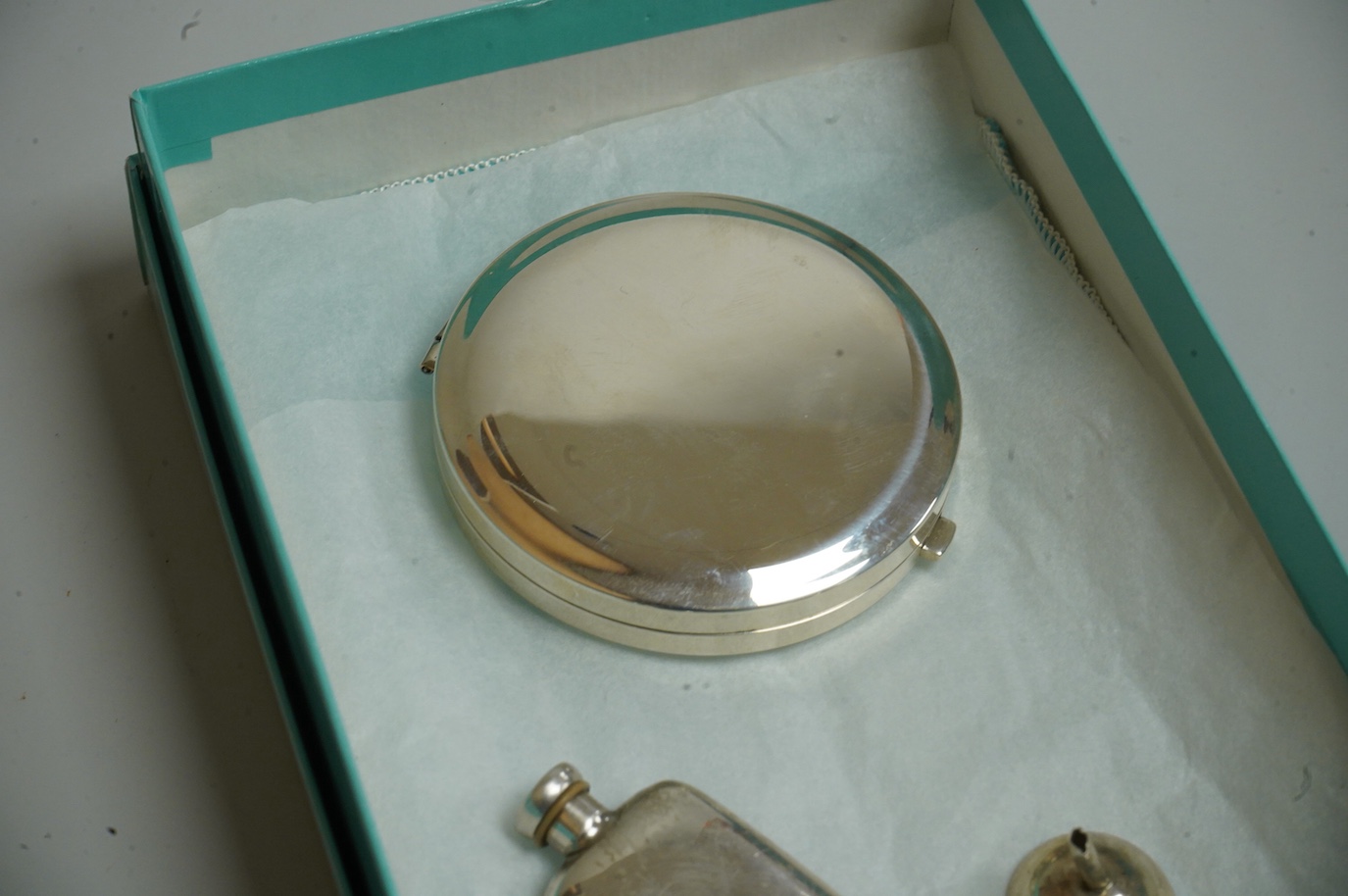 A small modern Tiffany & Co sterling scent flask, 44mm, together with a Tiffany & Co sterling compact, diameter 64mm and a small unmarked white metal funnel, with an associated Tiffany & Co box.